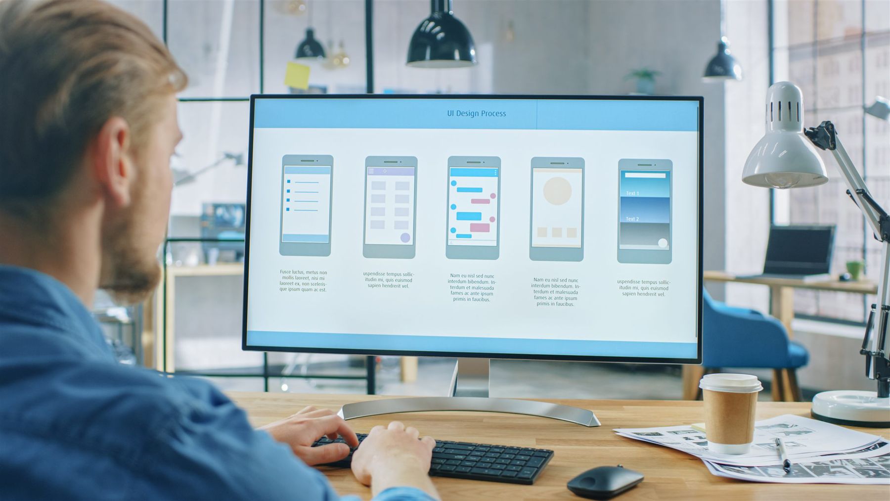 A designer at a desk reviewing interface layouts on a large monitor